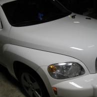 White car front quarter view in a dark garage, showing the headlight and hood.