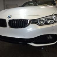 Front view of a white BMW sedan in a garage, showing the grille, headlights, and bumper.