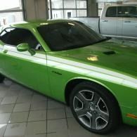Green Dodge Challenger parked indoors on a tiled floor, shown from the front side.