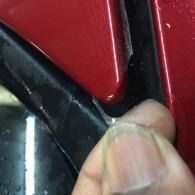 Thumb pressing a black plastic panel beside a red surface close-up