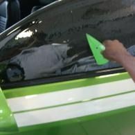 Hand washing a green and white car window with a green sponge