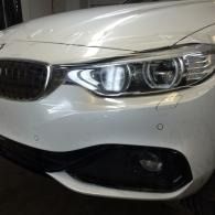 Front view of a white car’s headlight and grille, with a black lower bumper and fog light