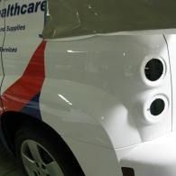 White car side panel with two circular taillights, partially covered in a garage