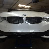Front view of a white BMW in a garage, showing the grille and headlights.