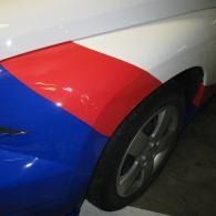 Close-up of a white, blue, and red car rear wheel and fender in a garage