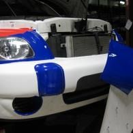 Front of a blue-and-white race car in a garage, with the hood open and exposed engine parts.