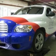 White car with blue front and red hood stripe parked in a garage