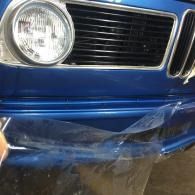 Close-up of a blue car front bumper with clear plastic wrap hanging over it.
