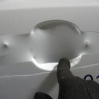 Gloved finger pointing at a dented white surface with a large circular indentation