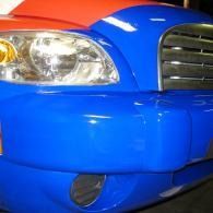 Close-up of a blue car’s front bumper, headlight, and grille