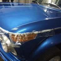 Blue car front end with damaged, taped headlight and crumpled hood