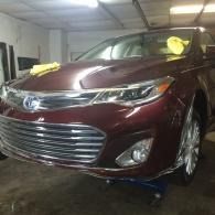 Maroon sedan in a garage, with a chrome grille and yellow cloths on the windshield.