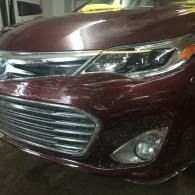 Front view of a maroon car with chrome grille and headlights, parked indoors.