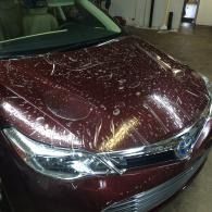 Maroon car hood covered in clear bubbled up wrapping inside a garage