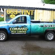 Blue pest control pickup truck with company branding parked beside a container type building