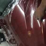 Close-up of a glossy red car body panel wrapped in clear plastic film