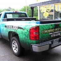 Green pickup truck with “COMMAND PEST” branding parked outside a building.