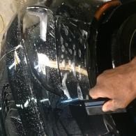 Hand polishing a black car’s chrome trim with a cloth at night.
