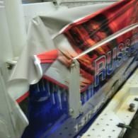 Partially covered red-and-blue arcade machine cabinet with graphics on a white perforated surface