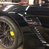 Black sports car close-up with dark alloy wheel and yellow brake caliper in a garage