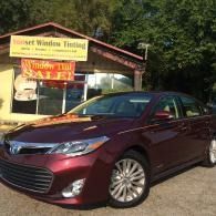 Maroon sedan parked outside a window tinting shop with a yellow sign.