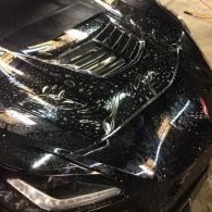 Black sports car hood with a damaged windshield and glossy reflections