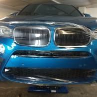 Front view of a blue BMW car in a garage, showing the grille and headlights.