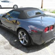 Gray convertible sports car parked in a driveway, rear view with black soft top and chrome wheels
