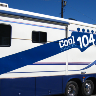White and blue trailer with Cool 104.7 logo, parked outdoors under a blue sky