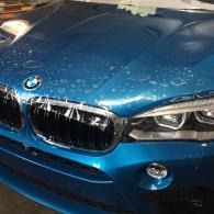 Blue BMW car front close-up with bubbled up clear wrapping on the hood and headlights visible