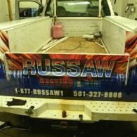 Pickup truck tailgate with a large “RUSSAW” tow/service sign and phone numbers.
