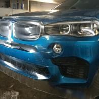 Close-up of a blue BMW front end with damaged grille and bumper in a parking garage