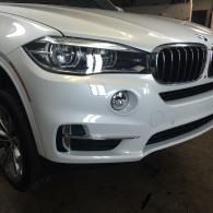 Front view of a white BMW SUV parked indoors, showing the grille and left headlight.