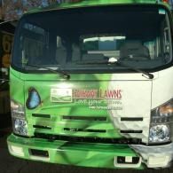 Green-and-white landscaping truck with company logo parked outdoors, front view