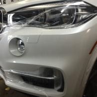 Front-left view of a white car’s bumper, headlight, and fog light in a garage