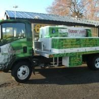 Green utility truck with a white cargo bed parked outdoors on a gravel lot