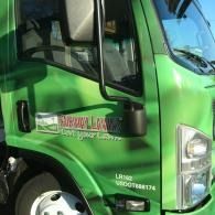 Green tow truck cab with company logo and chrome side mirror close-up