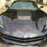 Front view of a black Chevrolet Corvette with red hood stripes parked outdoors.