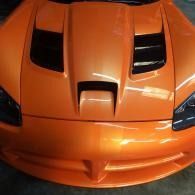 Orange sports car front with black hood vents and headlights