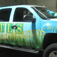 Blue landscaping company pickup truck with green and yellow logo and grass graphics on the side