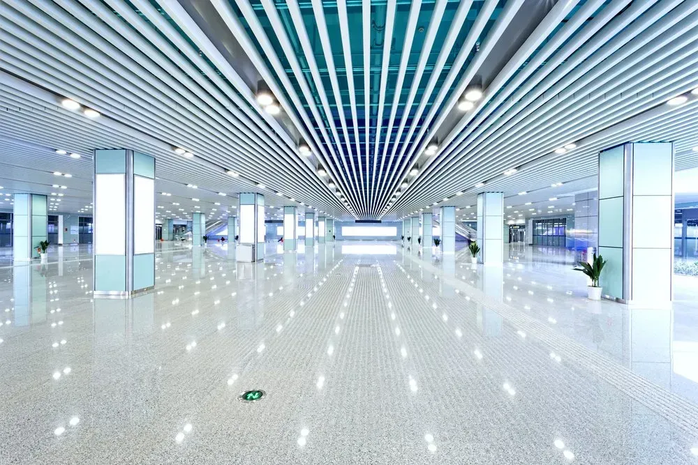Wide, glossy-floored building interior with multiple pillars, reflective ceiling, and bright, modern lighting.