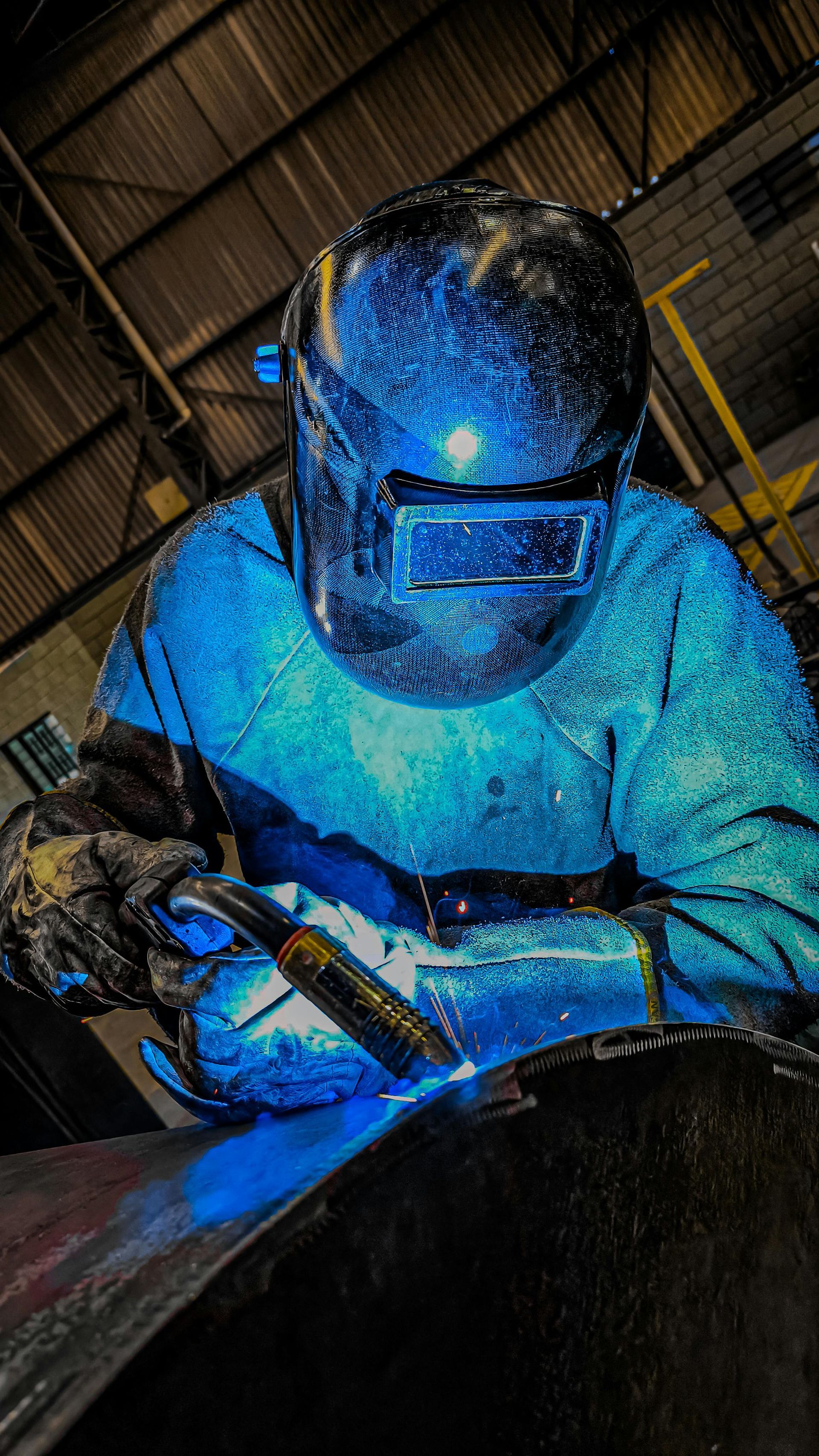 Welder in blue protective gear, working with bright sparks on metal.