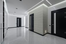 Modern hallway with black doors, white walls, and a patterned accent wall, lit by linear ceiling lights and a glossy floor.