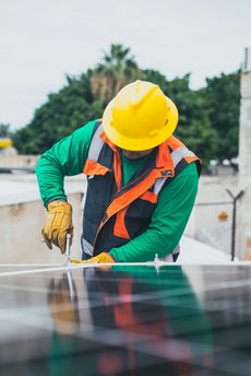Construction worker in yellow hard hat, installing solar panels on rooftop.