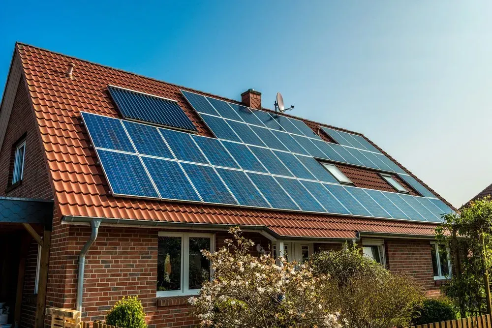 Solar panels on a red-tiled roof of a brick house against a blue sky.