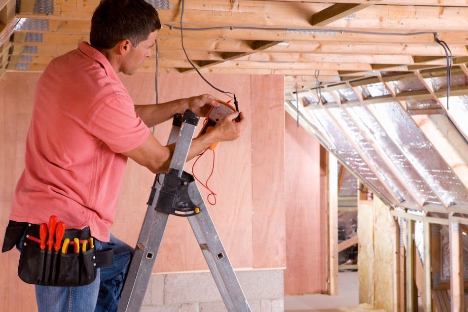 Man in pink shirt wiring electrical system from a ladder in a construction site.