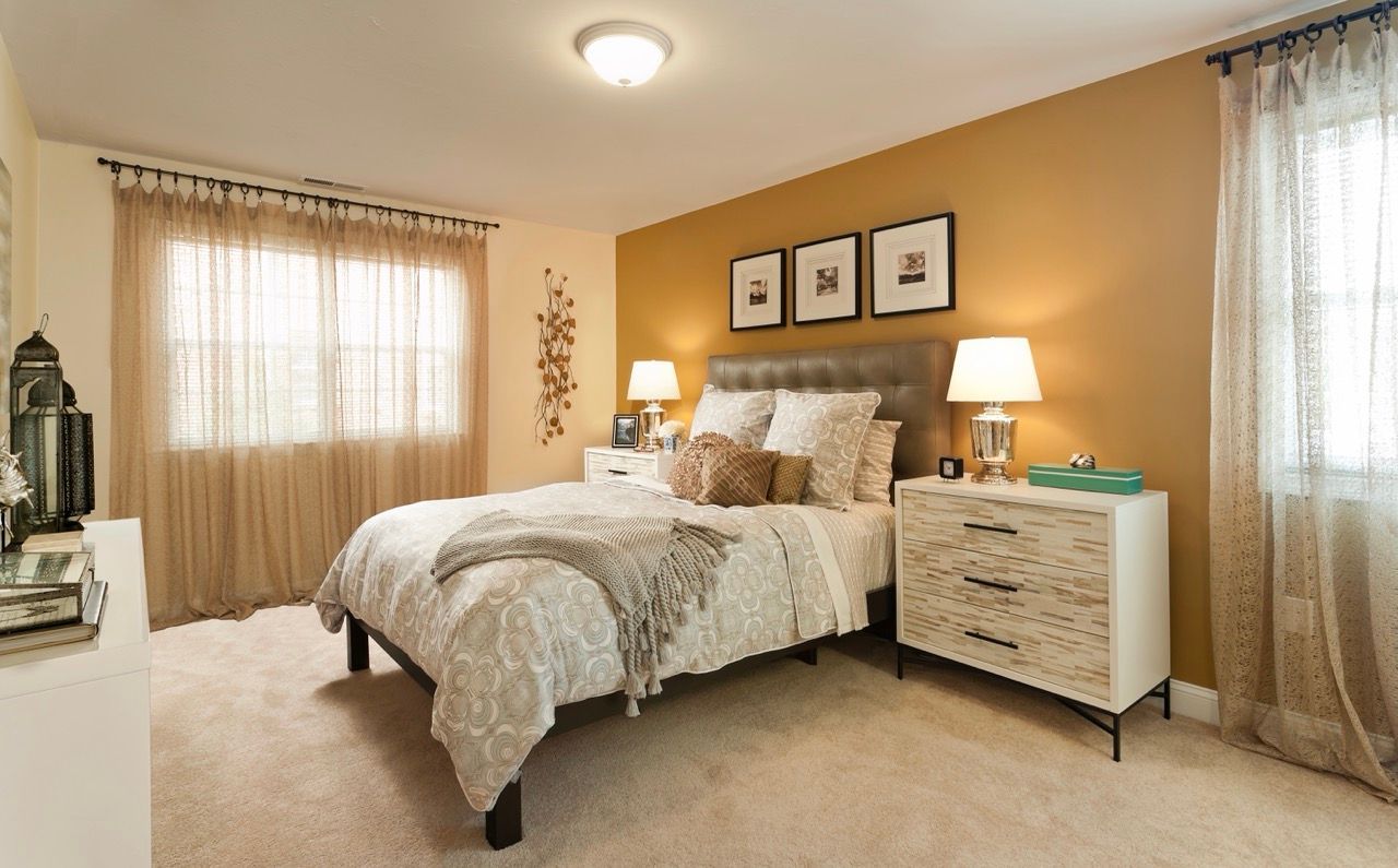 Bedroom in a modern apartment with a tufted headboard, two nightstands, lamps, and sheer beige curtains.