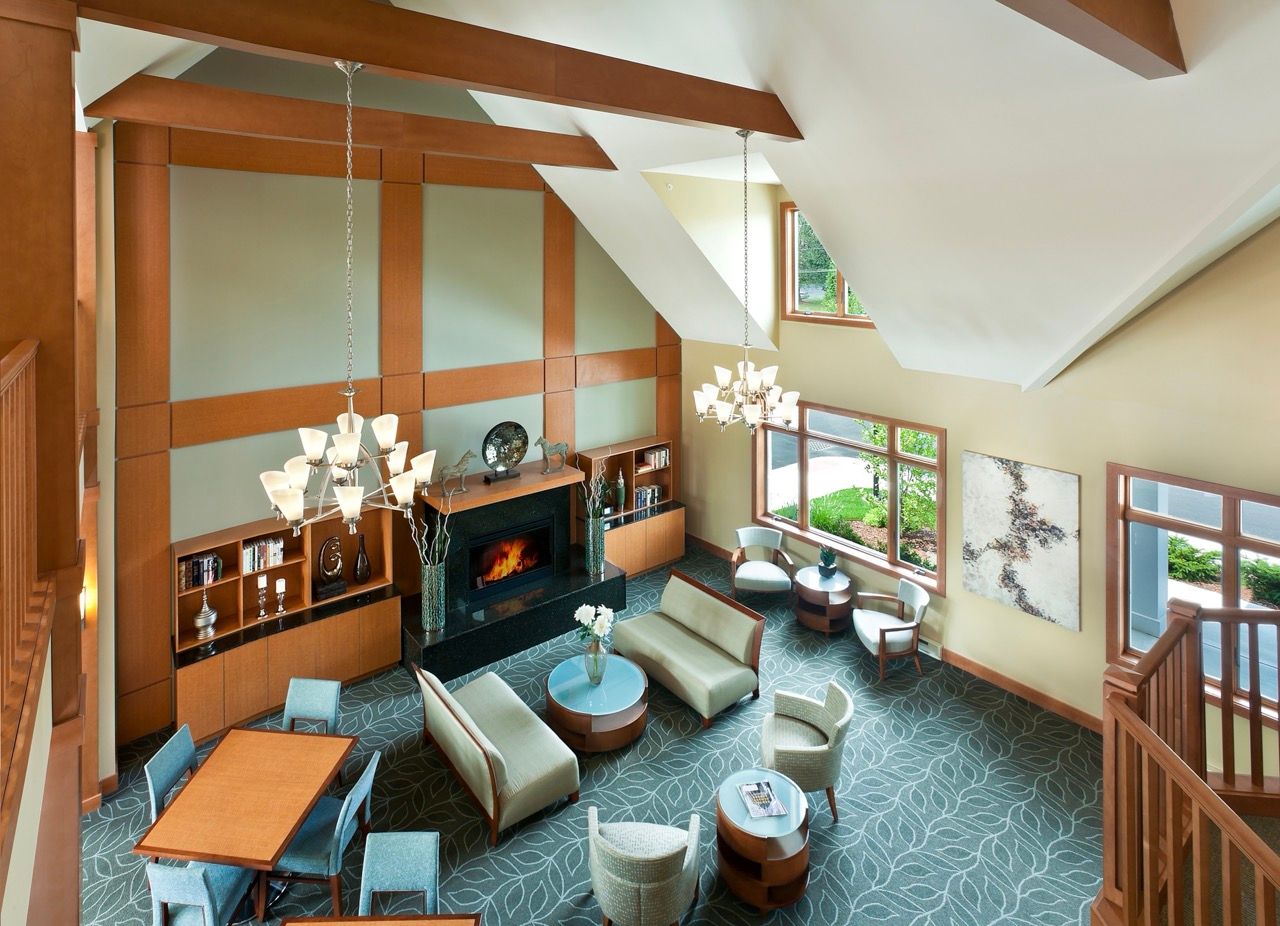 Two-story community lounge with a fireplace, chandeliers, bookshelves, and ample seating.