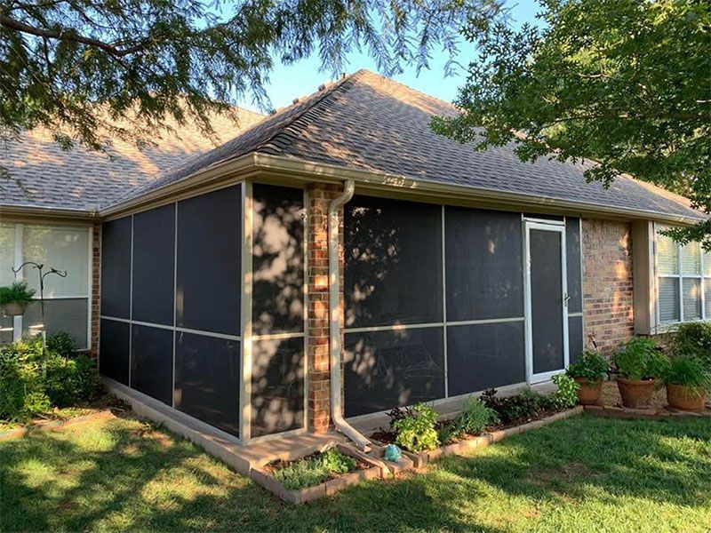 Screened porch attached to a brick house with dark screens, plants, and a white door.