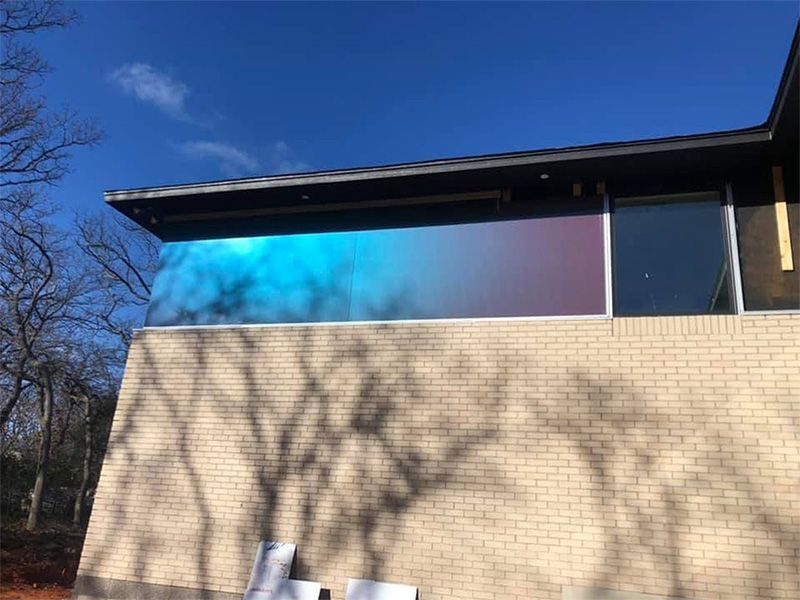 Exterior view of a brick building with large windows reflecting blue and purple colors, under a clear blue sky.